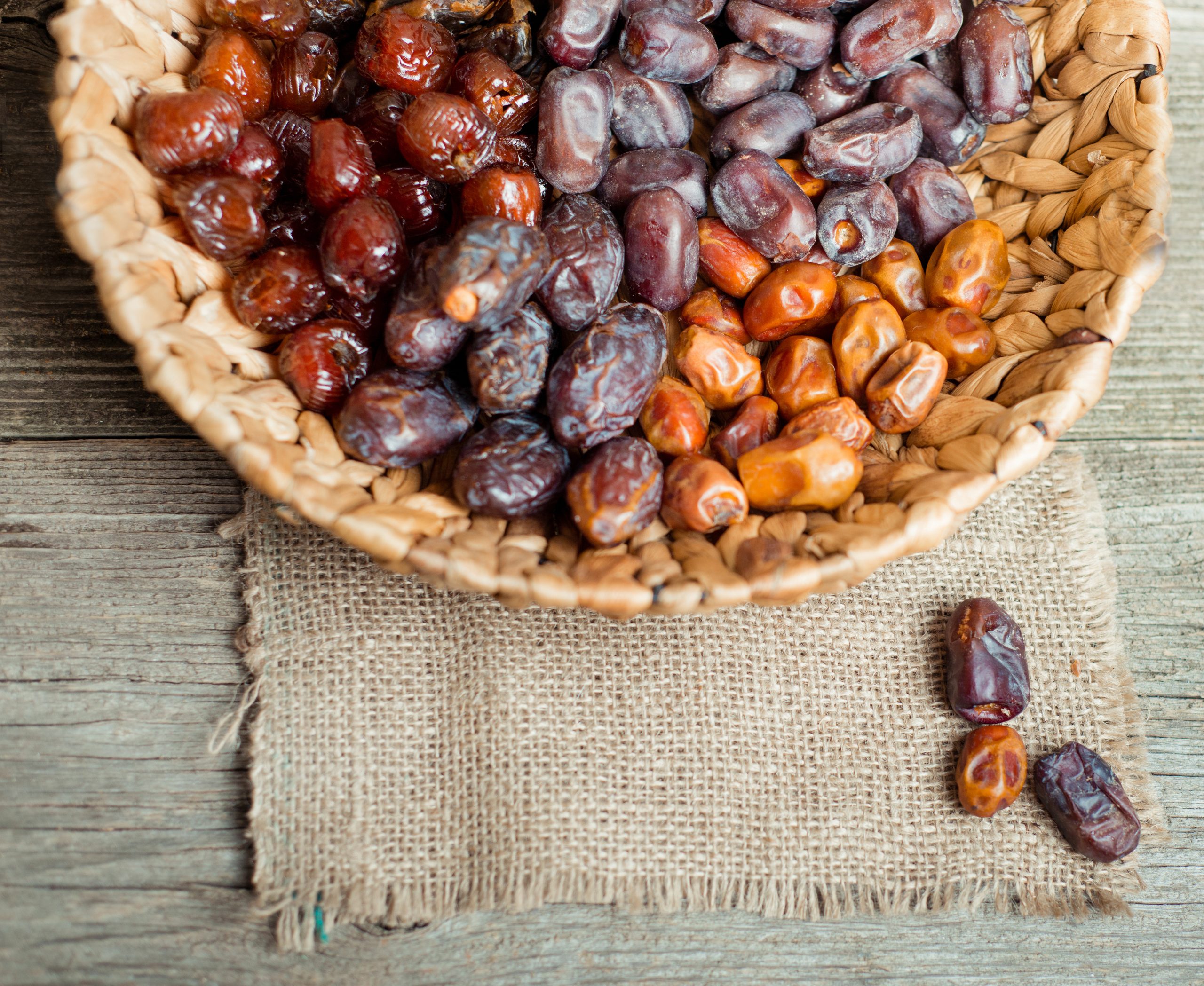 Dried dates in wicker basket on a wooden background, top view