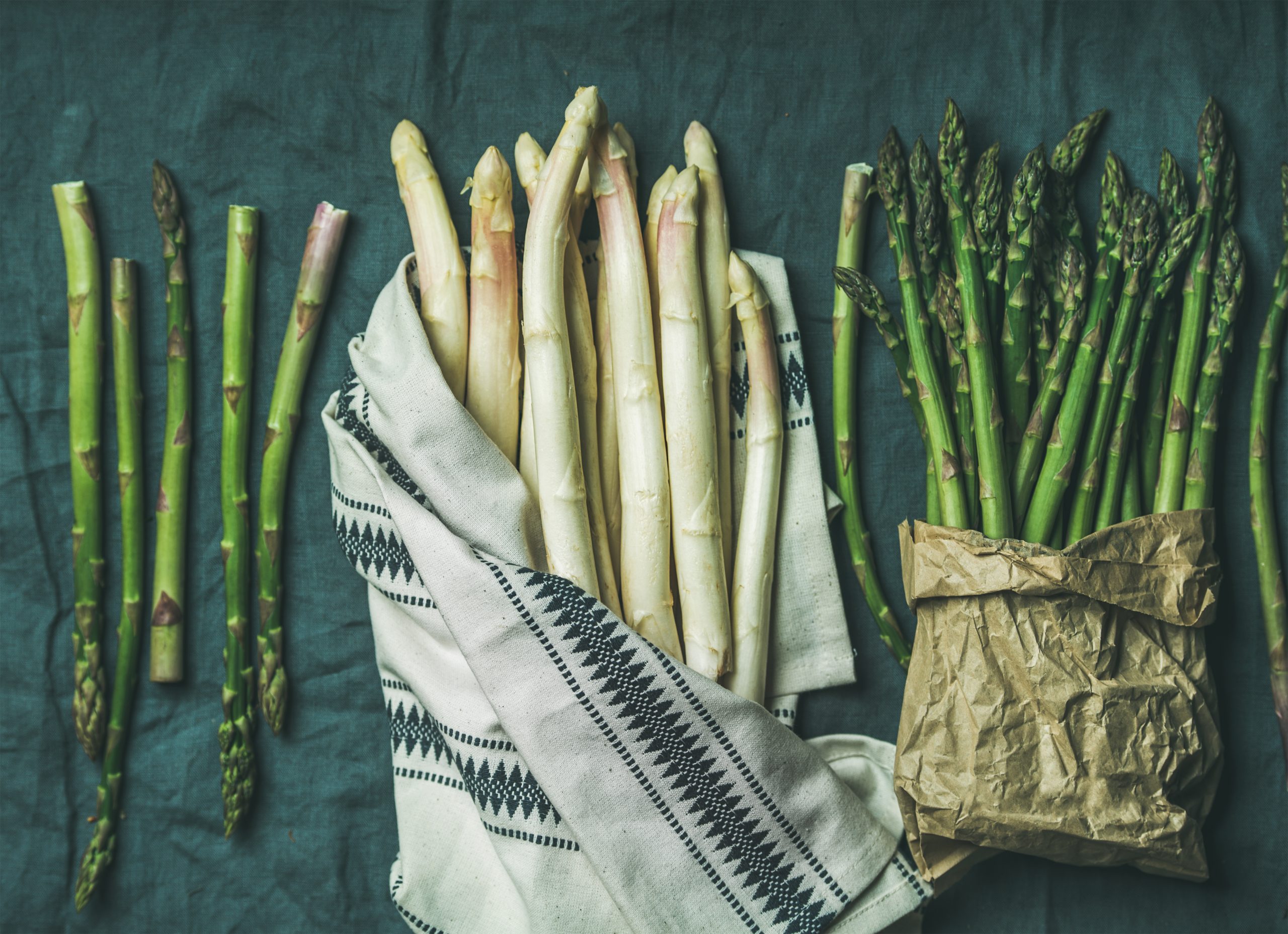 Fresh green and white asparagus in towel, grey background